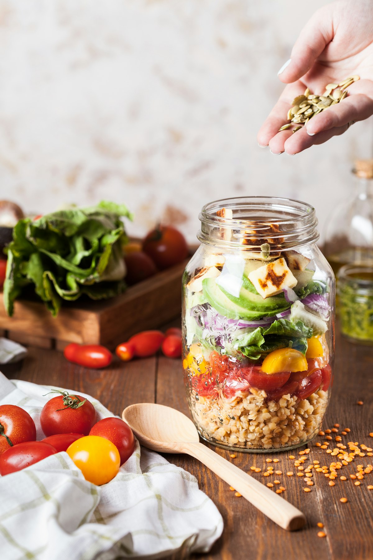 A mason jar salad layered with grains, tomatoes, avocado and pumpkin seeds